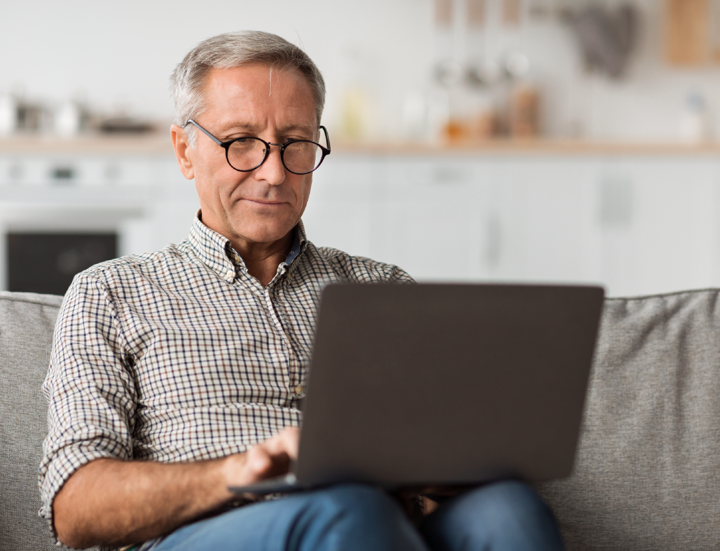 senior-male-using-laptop-sitting-on-couch-at-home-2022-12-16-08-14-23-utc-cropped